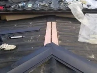 軒先に近い箇所から棟板金を順に被せ固定して棟板金工事する風景